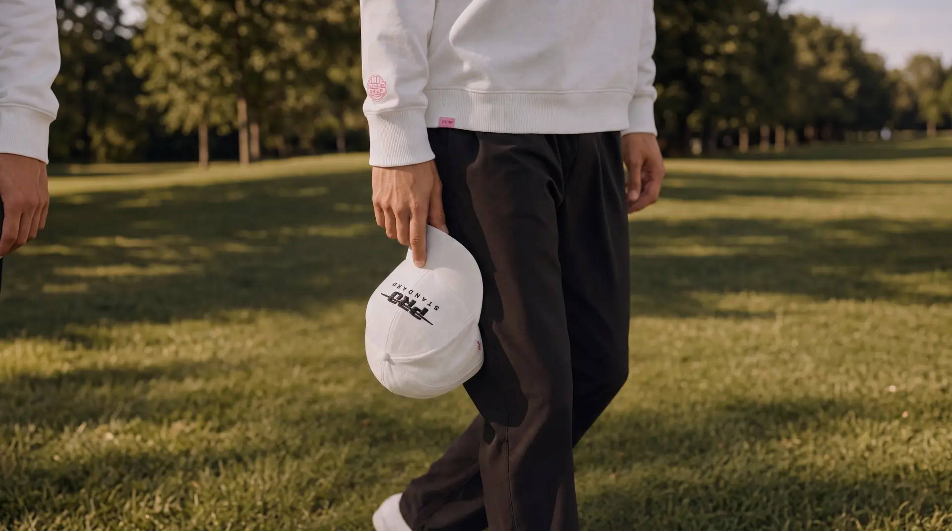 Model walking a sunlit fairway holding a white Pro Standard cap