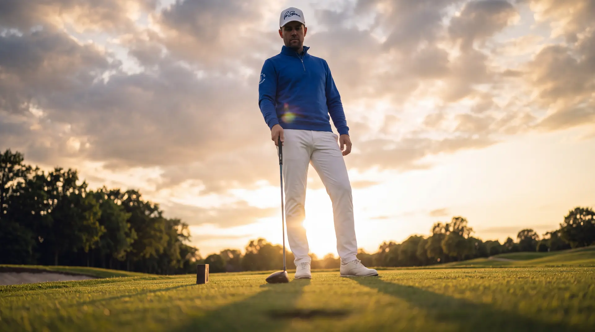 Model in a royal blue quarter-zip standing over a driver at sunset